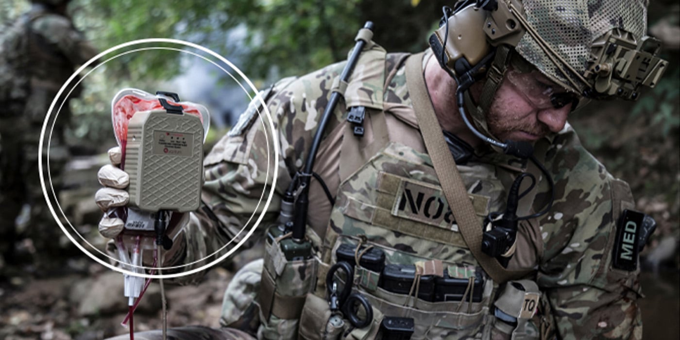 A soldier in camouflage gear administers medical treatment using a blood transfusion kit. The soldier wears protective headgear and carries various medical equipment, with a "MED" patch visible on the uniform.