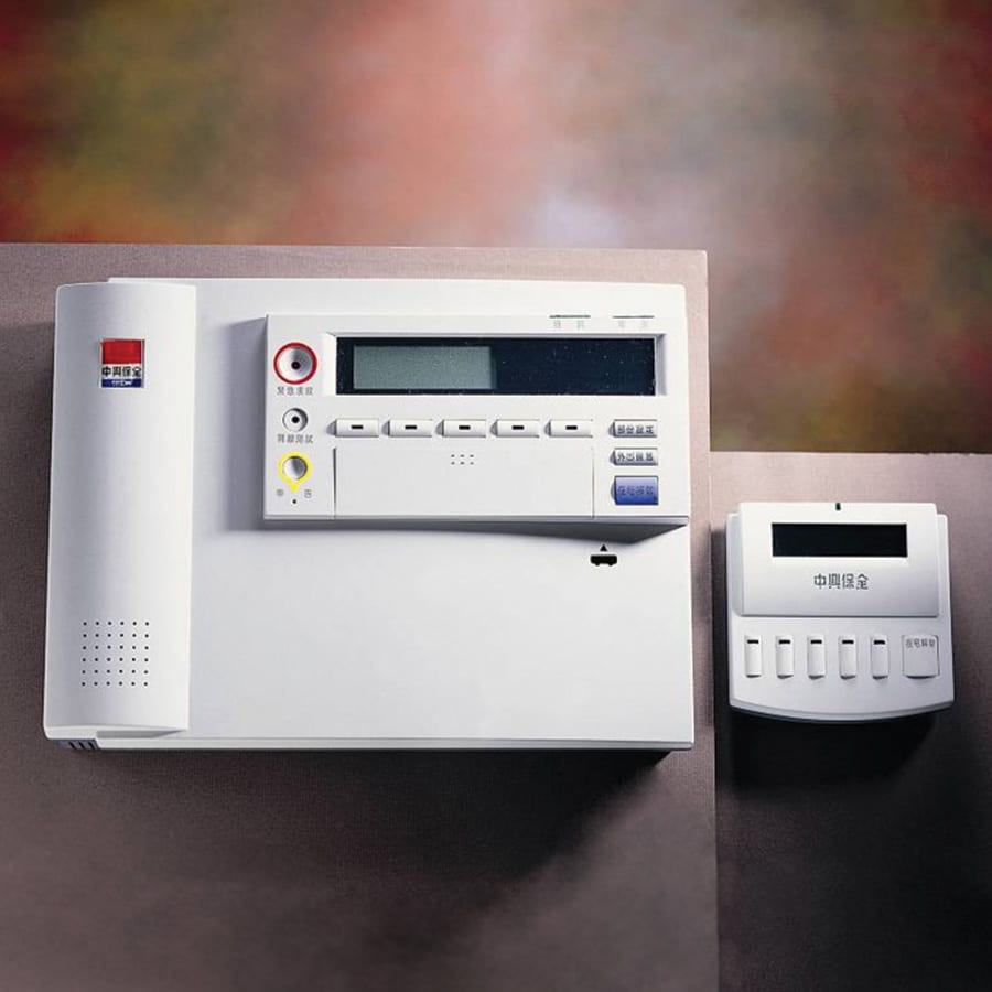 A wall-mounted white security control panel with an attached keypad and display screen next to a separate, smaller control unit.