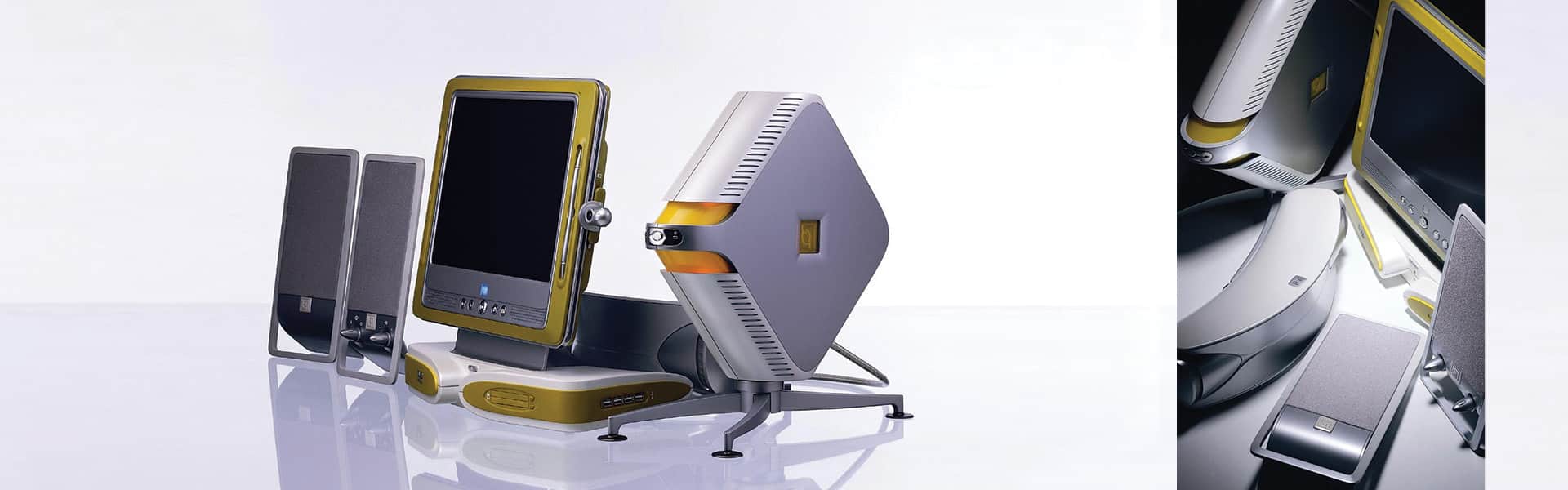 An angled view of a vintage desktop computer setup with two speakers, a flat screen monitor, and a distinctive, triangular CPU tower, all in a modern design with metallic finishes.