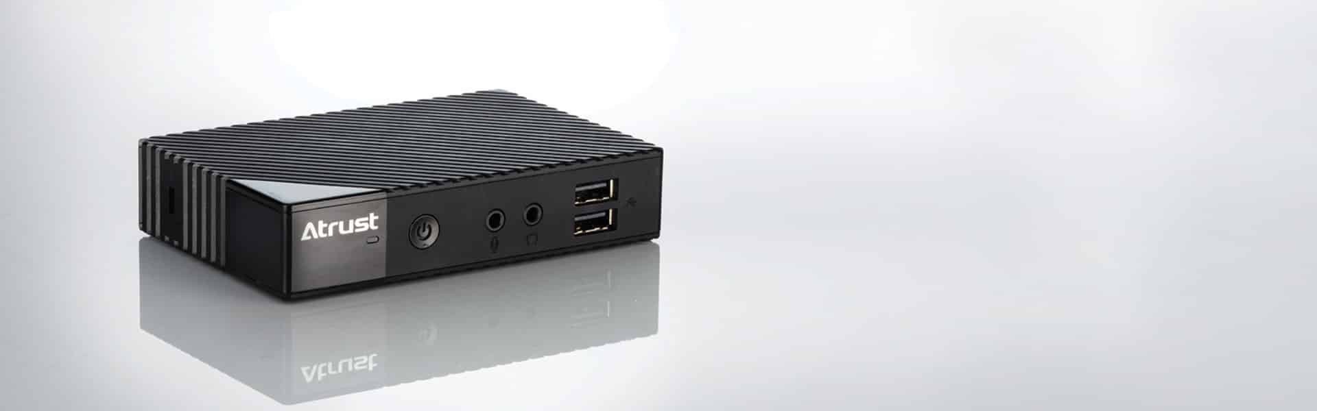 A black Atrust electronic device with multiple input ports, including USB, HDMI, and audio jacks, sits on a reflective surface.