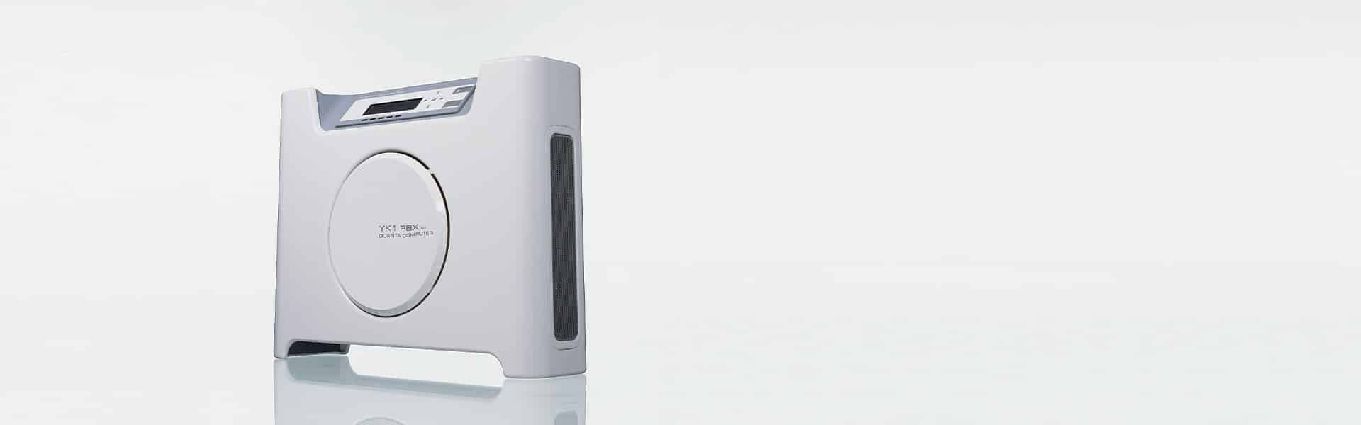 A compact, white digital device with a central circular panel and small display screen, standing on a white surface against a light background.